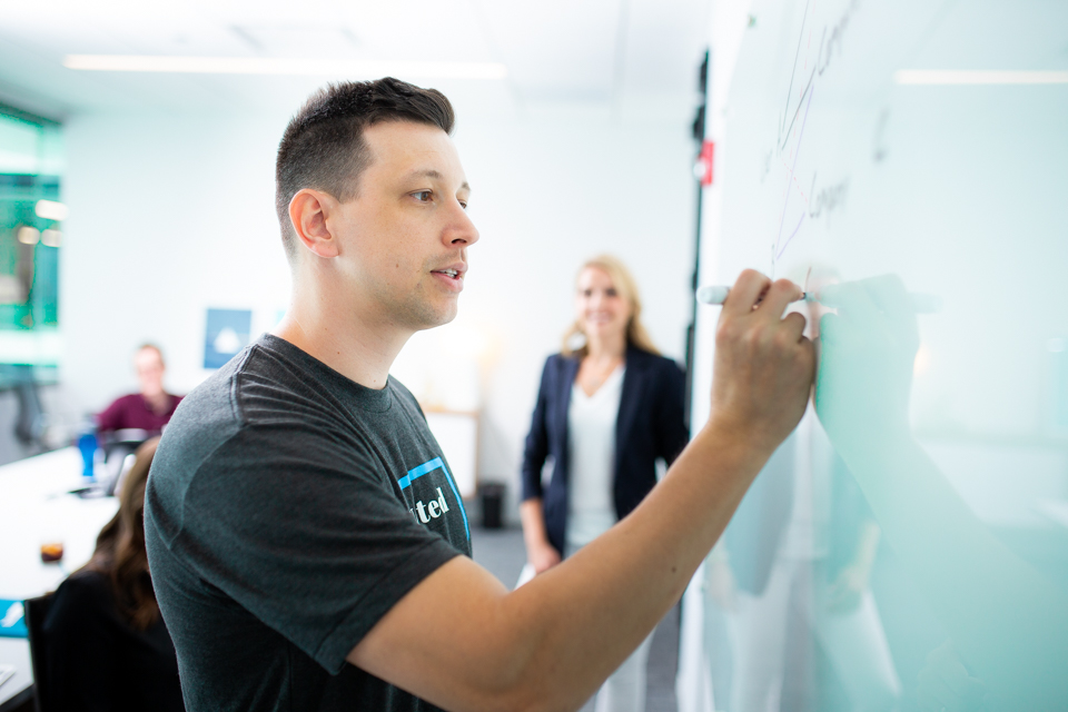 Adam Calica writes on a whiteboard in a conference room meeting.