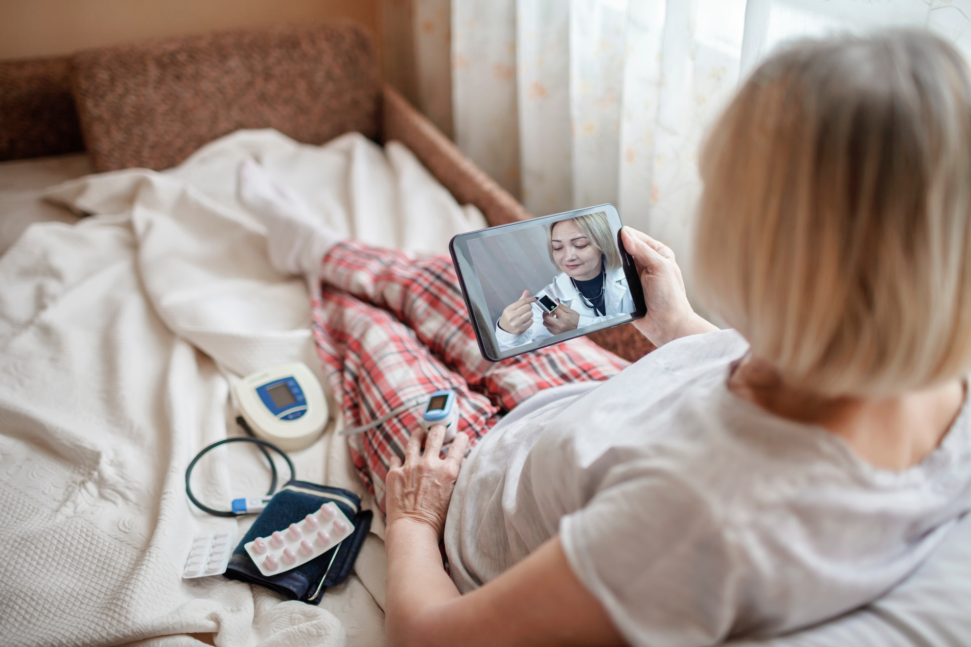 Old woman in bed looking at screen of laptop and consulting with a doctor online at home
