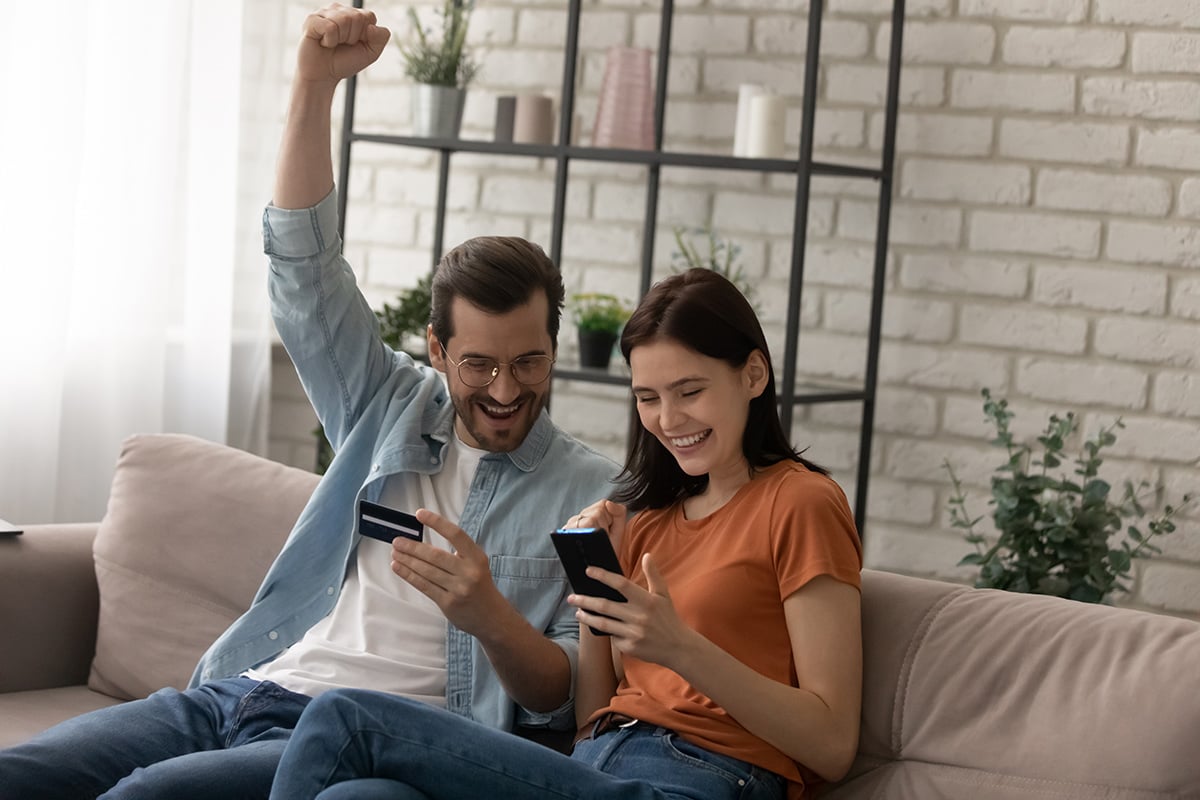 A couple sitting on a couch doing online shopping on a mobile phone