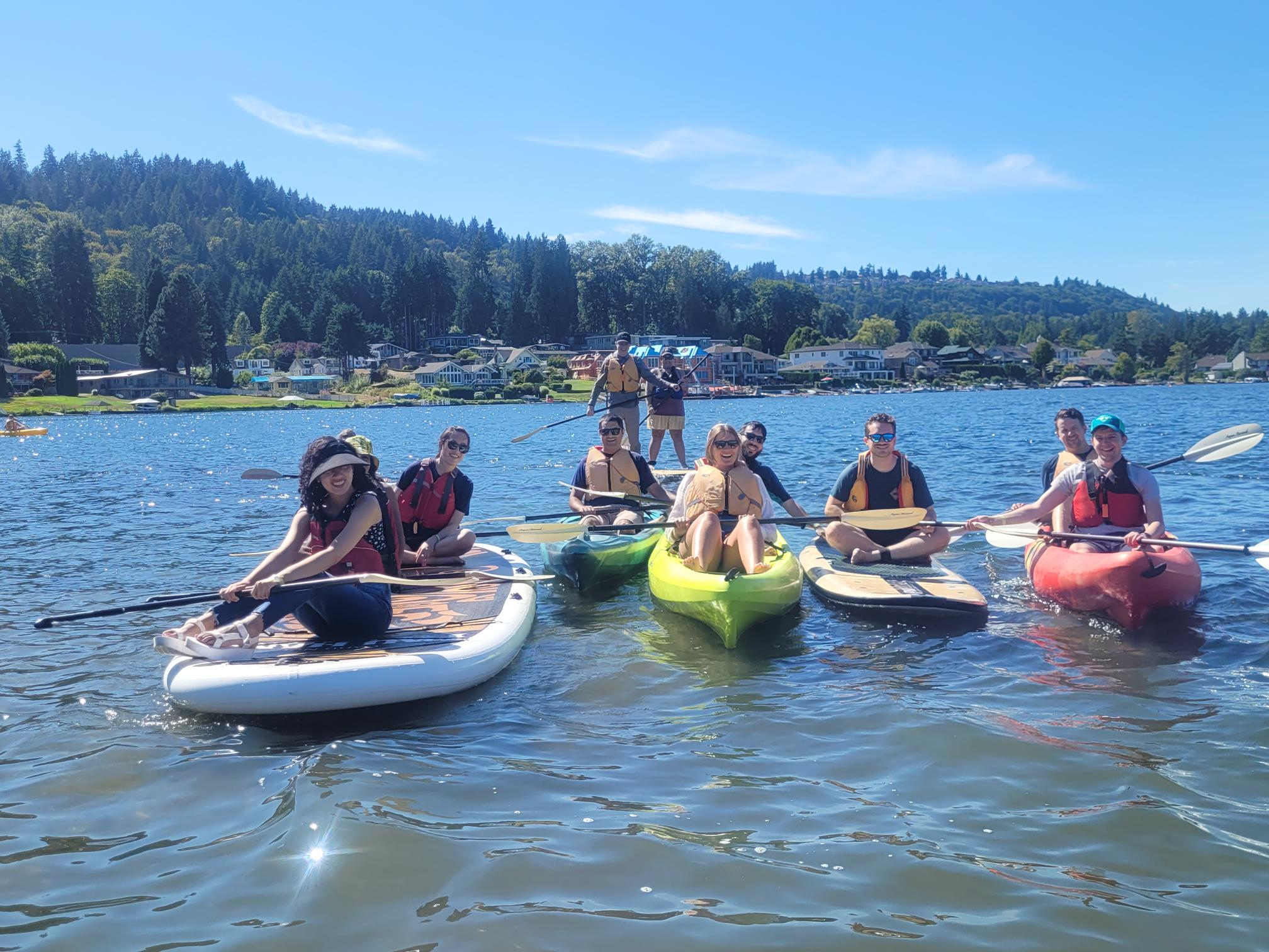 A group of Clean Power Research employees post for a photo while floating on paddleboards and in kayaks. 